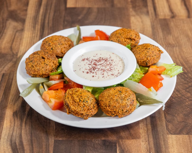 A white plate with six falafel balls, a side salad, and a bowl of tahini sauce.