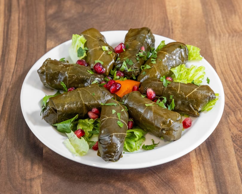 Grape leaves stuffed with rice and herbs, garnished with pomegranate seeds and parsley on a white plate.