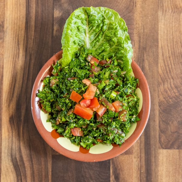 A vibrant tabbouleh salad with fresh parsley, tomatoes, and lettuce in a brown bowl on wood.