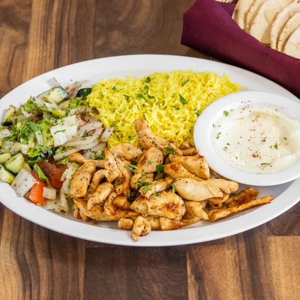 Chicken shawarma plate with yellow rice, salad, and garlic sauce, with pita bread in the background.