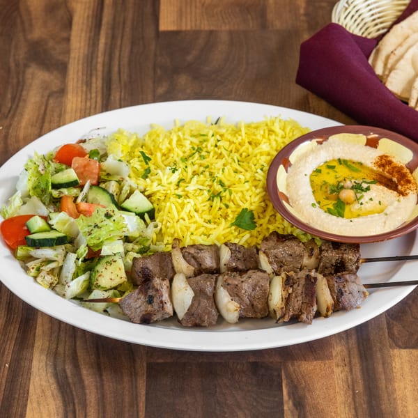 Beef shish kabob plate with yellow rice, salad, hummus, and pita bread on a wooden table.