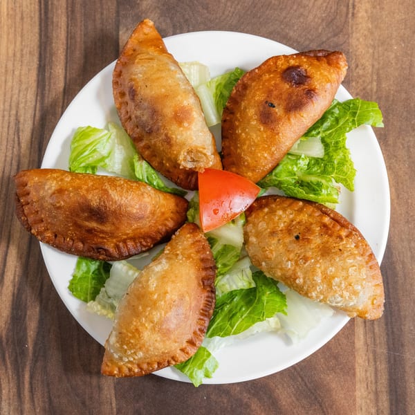 Five golden-brown empanadas arranged on a white plate with lettuce and a tomato wedge.